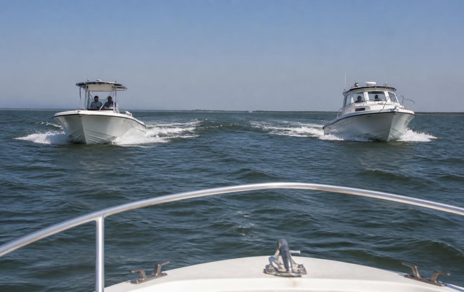 Two small motorboats approaching each other on open water seen from a third boat's bow