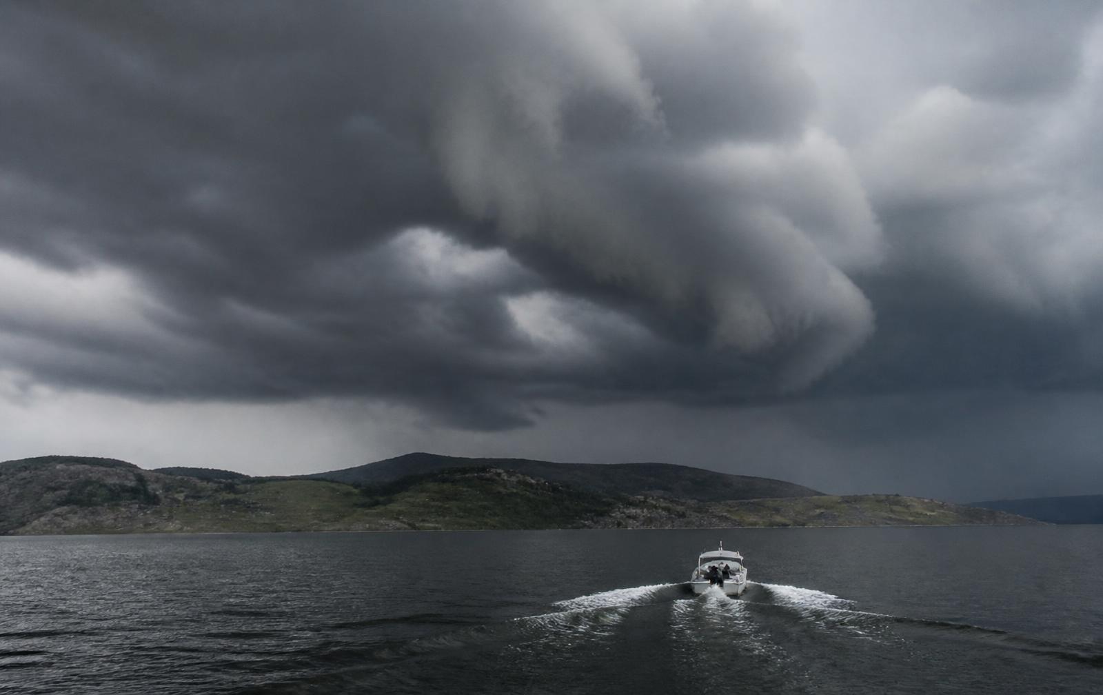 Dark storm clouds building over a lake with a small boat running back toward shore