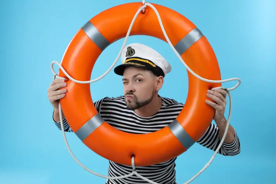 A boater in a striped shirt and captain's hat peering through an orange life ring.