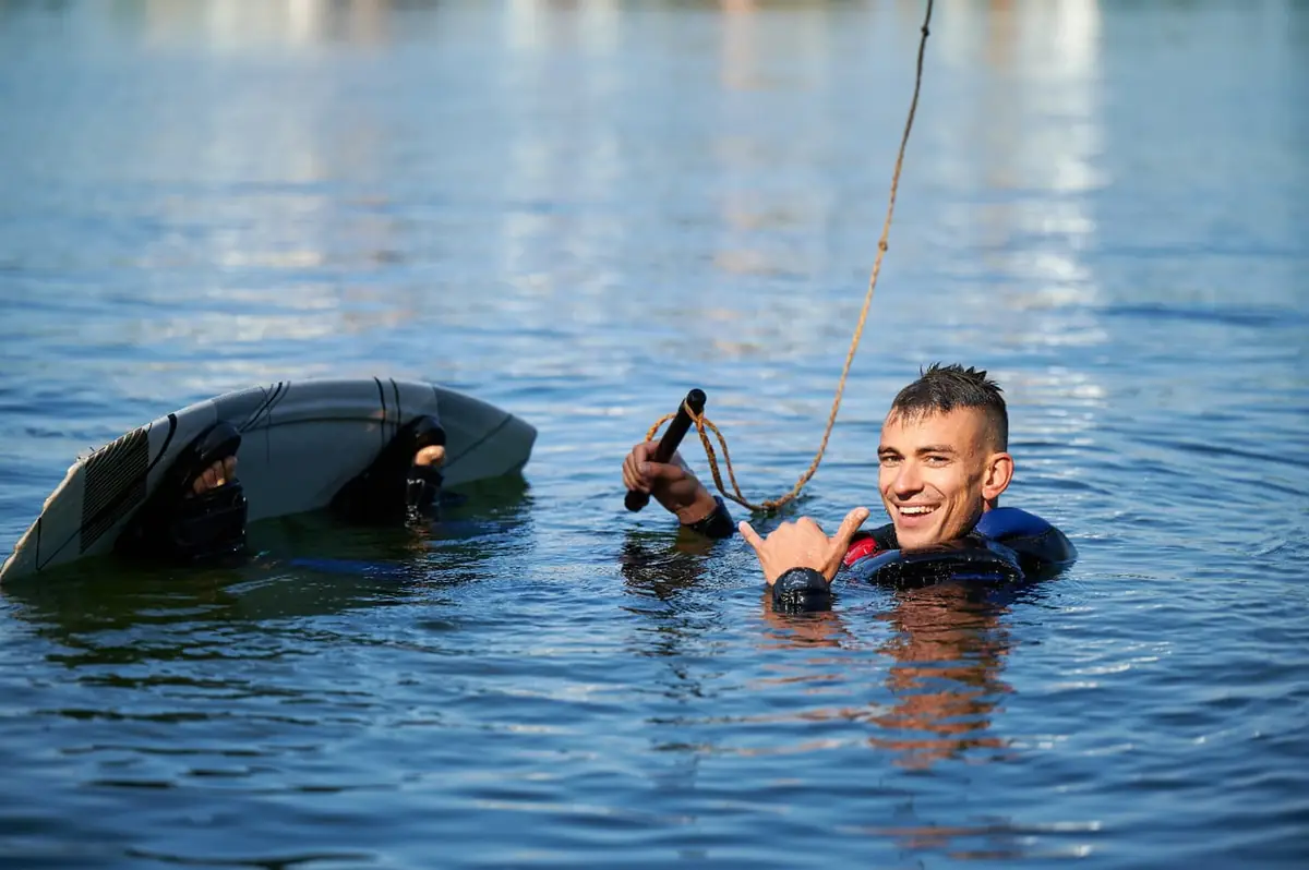 A wakeboarder in the water giving a shaka sign.